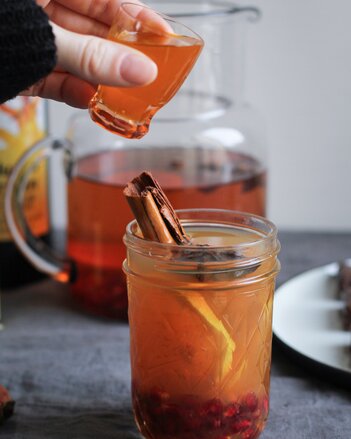 Auf dem Foto ist ein Glas mit Kurkuma Gewürz Drink zu sehen. Darin erkennt man Granatapfel kerne, Zitronenscheiben, Sternanis und eine Zimtstange. | © SONNENTOR