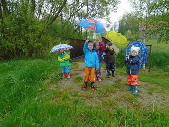 Auf dem Foto sind die Kinder in Regenkleidung und Regenschirmen zu sehen. | © SONNENTOR