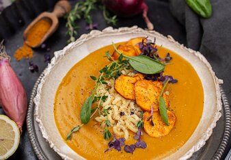 Auf dem Foto ist eine Schale Süßkartoffel-Kurkuma Suppe zu sehen. Darin sind Nudeln, Süßkartoffelchips und Spinatblätter zu sehen. | © SONNENTOR