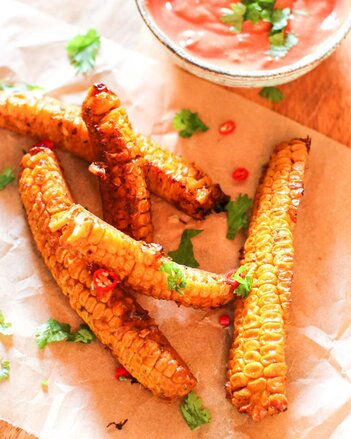 Foto von gegrillten Maiskolben. Neben den BBQ Corn Ribs sind auch frische Kräuter und ein Dip zu sehen. | © SONNENTOR
