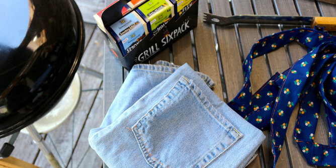 Jeans Grillschürze | © SONNENTOR Auf dem Foto ist eine Jeans zu sehen. Daneben steht das Grill Sixpack und auch ein Griller ist zu sehen. | © SONNENTOR