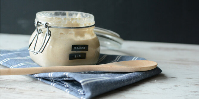 Sauerteig | © SONNENTOR Auf dem Foto ist ein Glas mit Sauerteig zu sehen. Davor liegt ein Holzkochlöffel. | © SONNENTOR