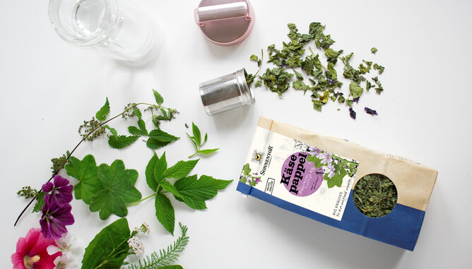 Käsepappel | © SONNENTOR Auf dem Foto sieht man eine SONNENTOR Packung Käsepappeltee. Daneben liegt ein Tee sieb mit den Kräutern darin. | © SONNENTOR