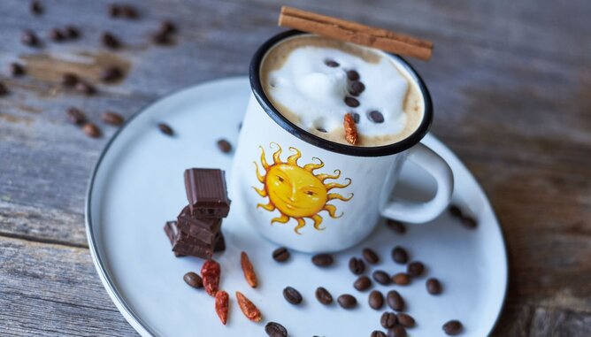 Nudelholz Kaffee Mexican Coffee | © SONNENTOR Auf dem Foto sieht man eine SONNENTOR Tasse mit Mexican Coffee darin. Daneben sind Schokostückchen, Chili und Kaffeebohnen zu sehen. | © SONNENTOR