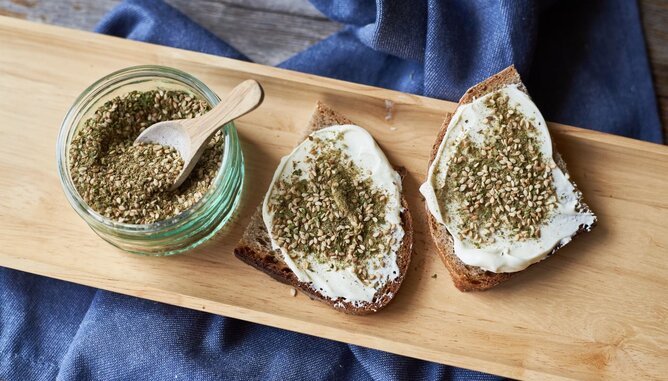 Zatar | © SONNENTOR Auf dem Foto sieht man Brot mit Aufstrich und Zatar darauf. Daneben steht ebenfalls ein Glas mit Zatar. | © SONNENTOR