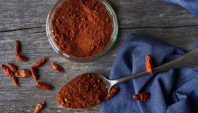 Baharat | © SONNENTOR Auf dem Foto sieht man ein Glas mit Baharat. Daneben liegt ein Löffel, ebenfalls mit Bahrat gefüllt. Auch Chilischoten sind zu sehen. | © SONNENTOR