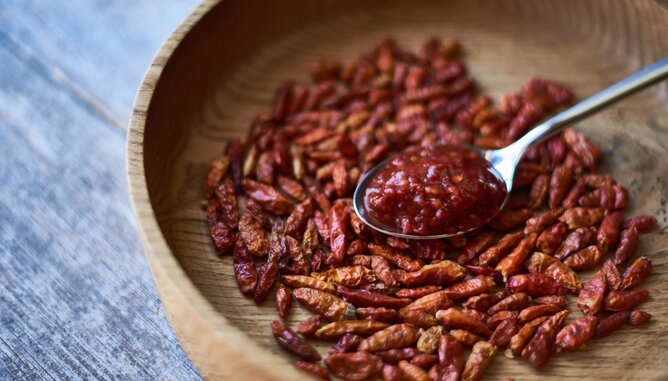 Harissa | © SONNENTOR Auf dem Foto sieht man eine Holzschale mit Chilischoten darin. Darauf liegt ein Löffel mi Harissa Paste. | © SONNENTOR