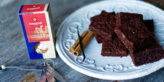 Lebkuchen Brownies | © SONNENTOR Auf dem Foto sieht man einen Teller mit Lebkuchenbrownies. Daneben liegt eine Zimtstange. Auch eine Packung Lebkuchengewürz ist zu sehen. | © SONNENTOR