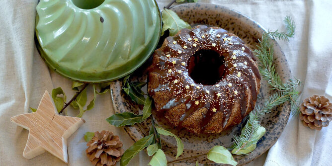 Gewürzkuchen | © SONNENTOR Auf dem Foto ist ein Gugelhupf mit Schokoglasur und goldenen Sternchen zu sehen. Daneben liegen Zweige und Zapfen. | © SONNENTOR