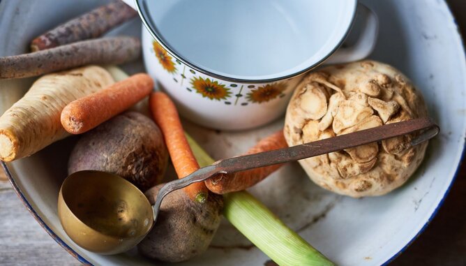 Nudelholz Suppe | © SONNENTOR Auf dem Foto sieht man einen Topf und daneben frisches Gemüse wie Pastinaken, Karotten und Sellerie. | © SONNENTOR