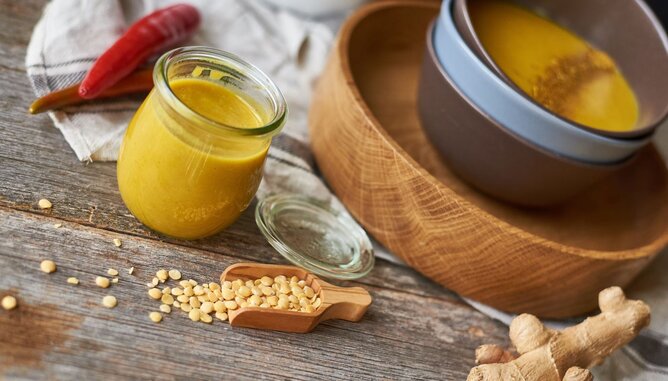 Nudelholz Suppe Linsen | © SONNENTOR Auf dem Foto sieht man einen Teller mit gelber Linsensuppe. Daneben sieht man frischen Ingwer, Linsen und Paprika. | © SONNENTOR