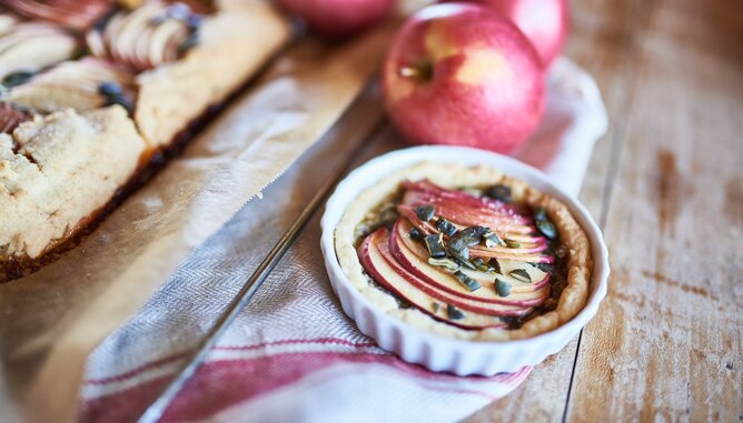 Apfel und Gewürze | © SONNENTOR Auf dem Foto sieht man ein kleines Apfelküchlein. Dahinter sieht man auch ganze Äpfel. | © SONNENTOR