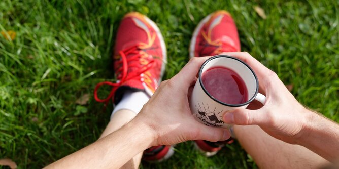 Sport Tee | © SONNENTOR Auf dem Foto sieht man einen Mann mit Sportschuhen. Er sitzt und trinkt eine Tasse Tee. | © SONNENTOR