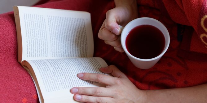 Lesen Tee | © SONNENTOR Auf dem Foto ist jemand mit einer Tasse Tee in der Hand zu sehen. Die Person liest ein Buch. | © SONNENTOR