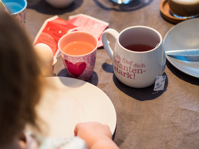 Familienfrühstück | © SONNENTOR Auf dem Foto sieht man ein Kind vor einem Teller und einer Tasse Tee sitzen. | © SONNENTOR