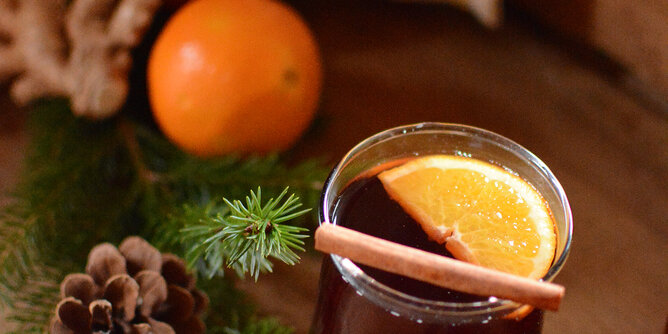 Kaminknistern mit Schuss | © SONNENTOR Auf dem Foto sieht man ein Glas mit Kaminknistern Punsch. Darin sieht man eine Orangenscheibe und eine Zimtstange. | © SONNENTOR