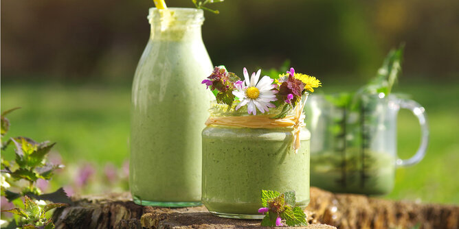 Basenfasten | © SONNENTOR Auf dem Foto sieht man zwei Gefäße mit grünem Smoothie darin. Sie sind mit Blüten gestaltet. | © SONNENTOR