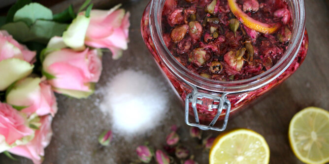 Valerie Walpurgis Rosensirup | © SONNENTOR Auf dem Foto sieht man ein Glas mit Rosensirup. Daneben sieht man Rosen, Zucker und Zitronenscheiben. | © SONNENTOR